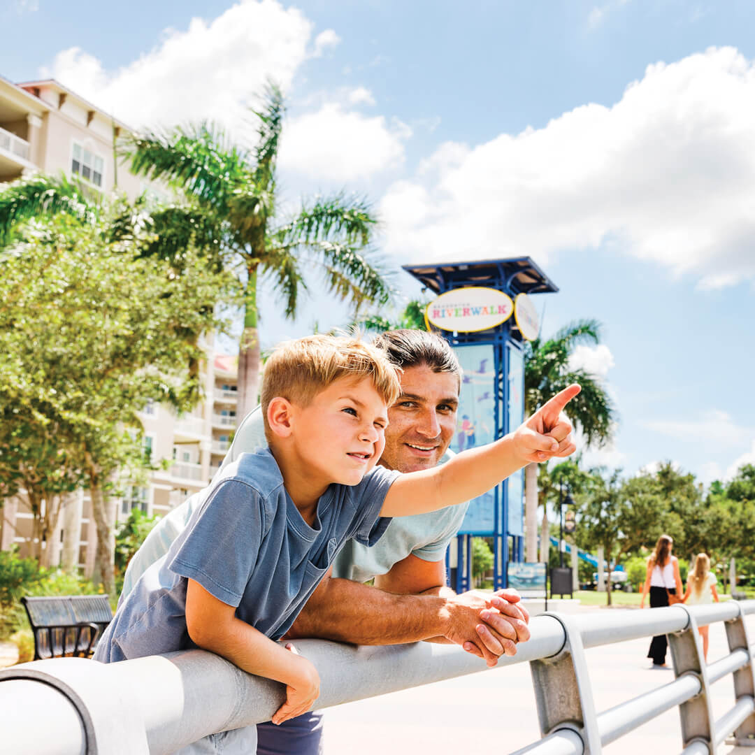 Home a man and son leaning on a railing on the Bradenton Riverwalk