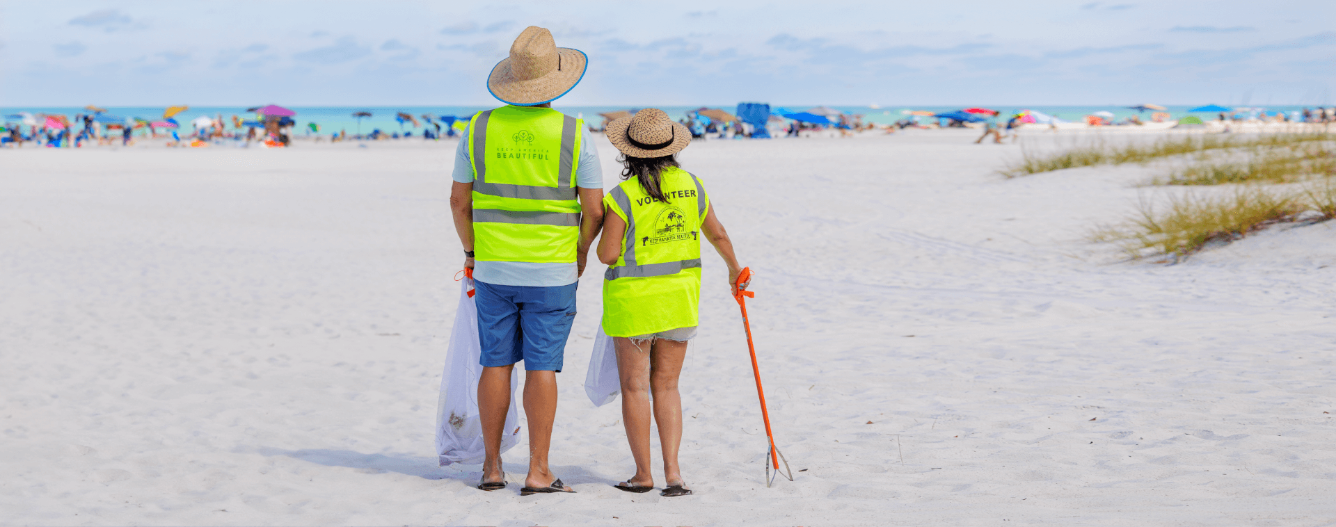 Love It Like A Local a man and woman in Keep Manatee Beautiful and Keep America Beautiful volunteer reflective vests, holding a trash picker on an anna maria island beach