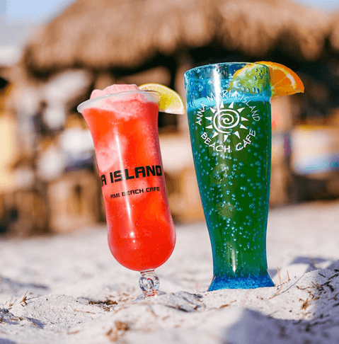 Beachside Bites: Top Toes-in-the-Sand Dining Destinations on Anna Maria Island two brightly colored drinks with anna maria island beach cafe logos on them in the sand