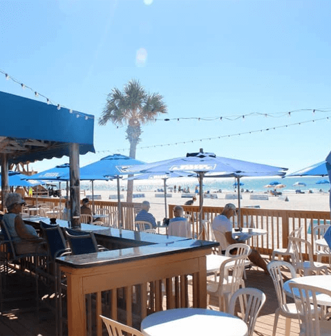 Beachside Bites: Top Toes-in-the-Sand Dining Destinations on Anna Maria Island blue umbrellas and white chairs and tables outside at Coquina Beach Cafe